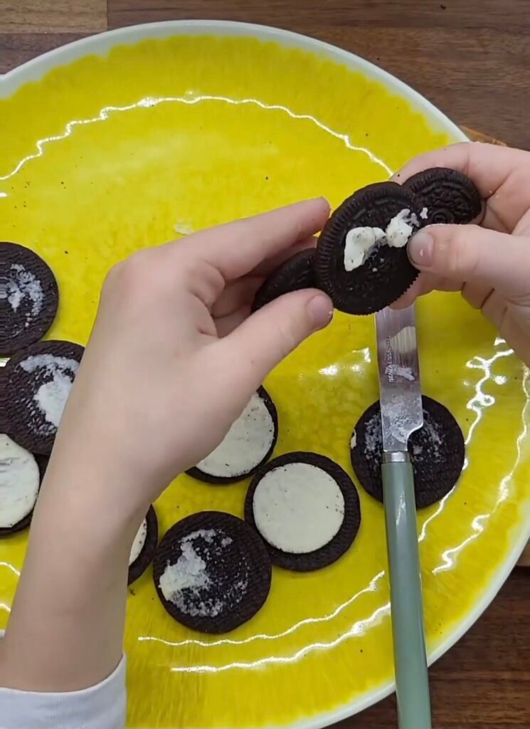 A child's hand pushes 2 halves of an oreo onto the back of another one to look like wings