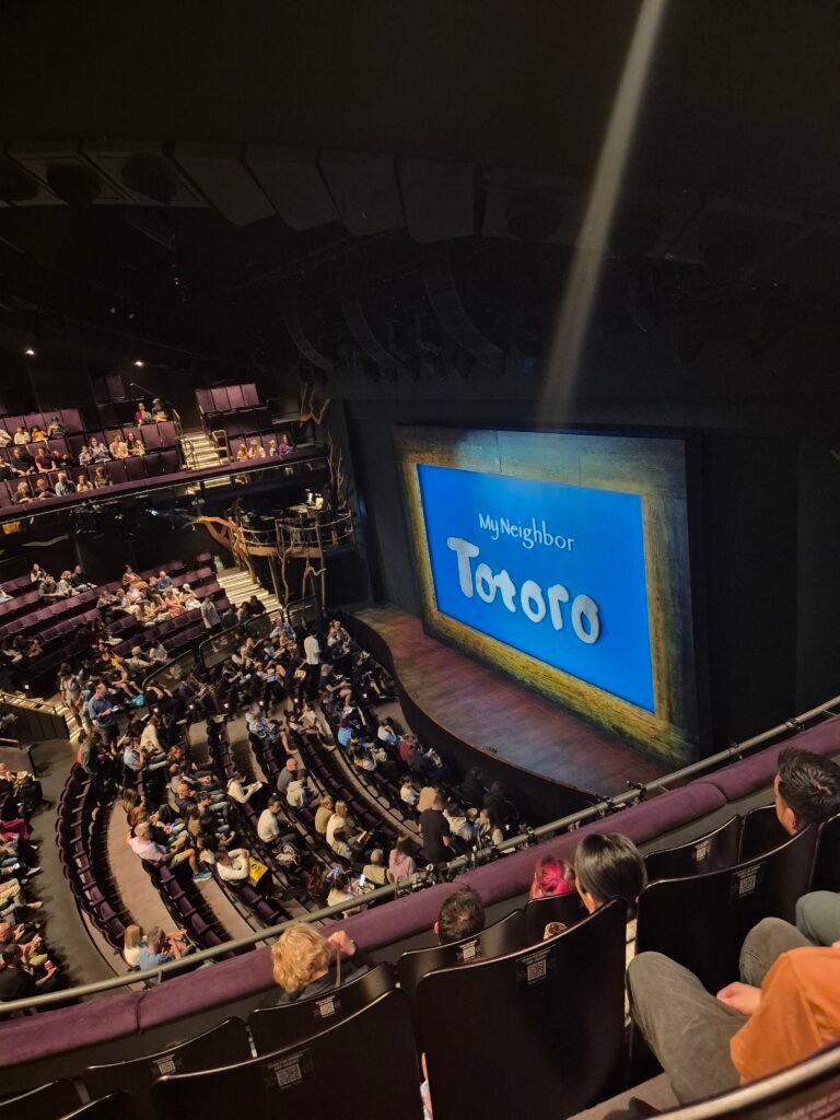 The photo is in a theatre and shows a view of the stage from a seat in the circle. There is a blue screen and the words my neighbour Totoro are written in white.