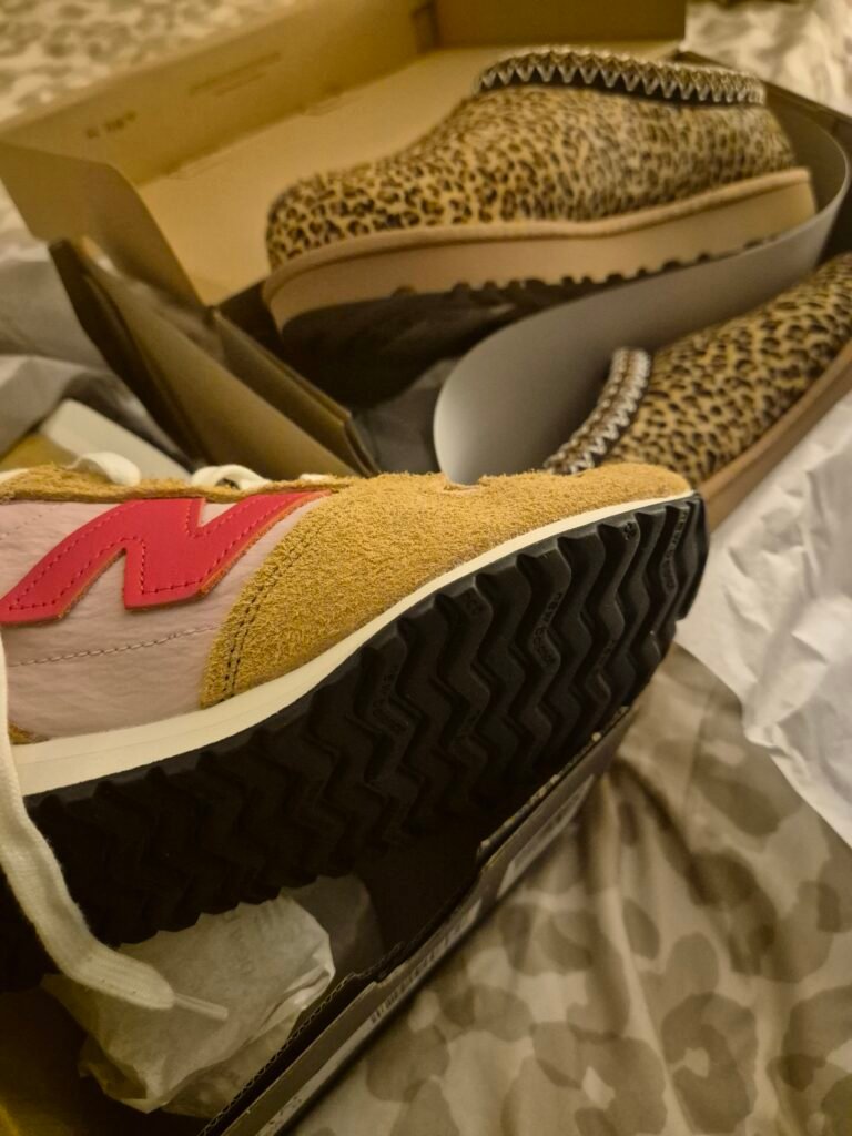 The image shows 2 pairs of shoes, each in a shoebox. The ones closest to the camera are the brand New balance, with a hot pink N, baby pink surround and a dark brown suede over the toe area and the sides of the laces. The pair behind are the Ugg slippers, they are a leopard print pattern.