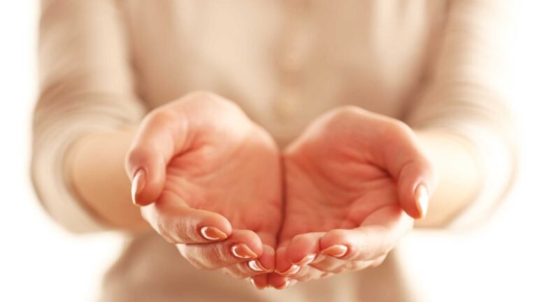 The forefront of the photograph is a woman's hands outstreched in front of her. Her body is visible wearing a light coloured button up top in the background, but her head is not visible.