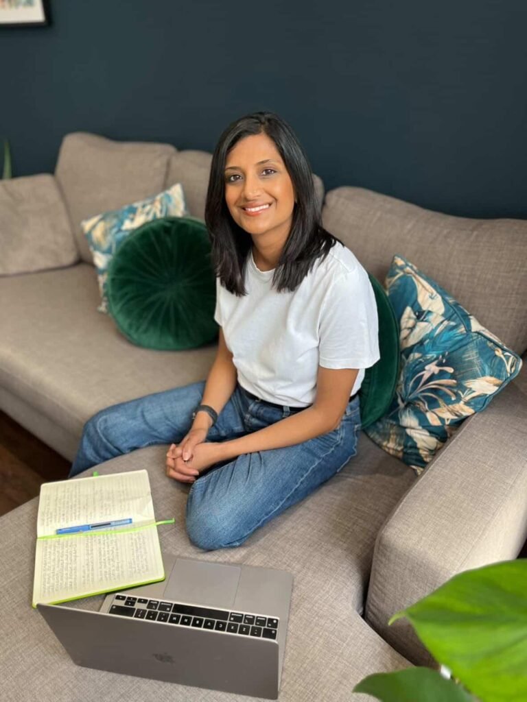 The image shows Priya Patel sitting on a grey corner sofa with a notebook and laptop.