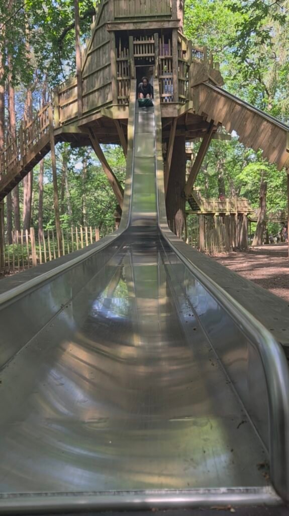 The photo is taken from the bottom of a large slide. At the top sits a young boy with his feet in a sack ready to slide down