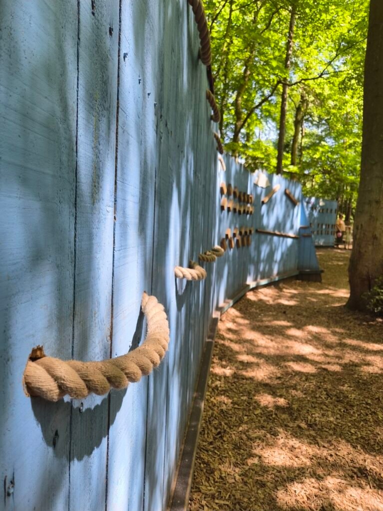 The photo shows a curvy climbing wall. It is a sky blue colour and all the grips are either made from wood or rope