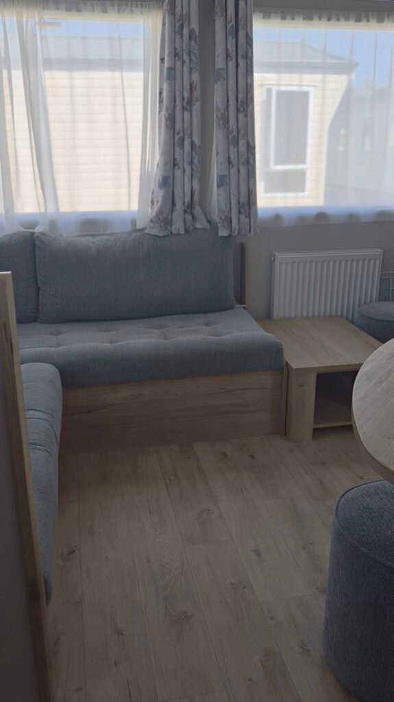The photo shows the living area of a bronze rated caravan. It looks fairly clean and tidy with a grey corner seating area and 2 windows