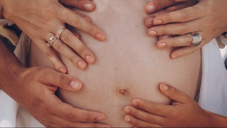 The photo shows the belly of a pregnant woman with several hands resting upon her bump